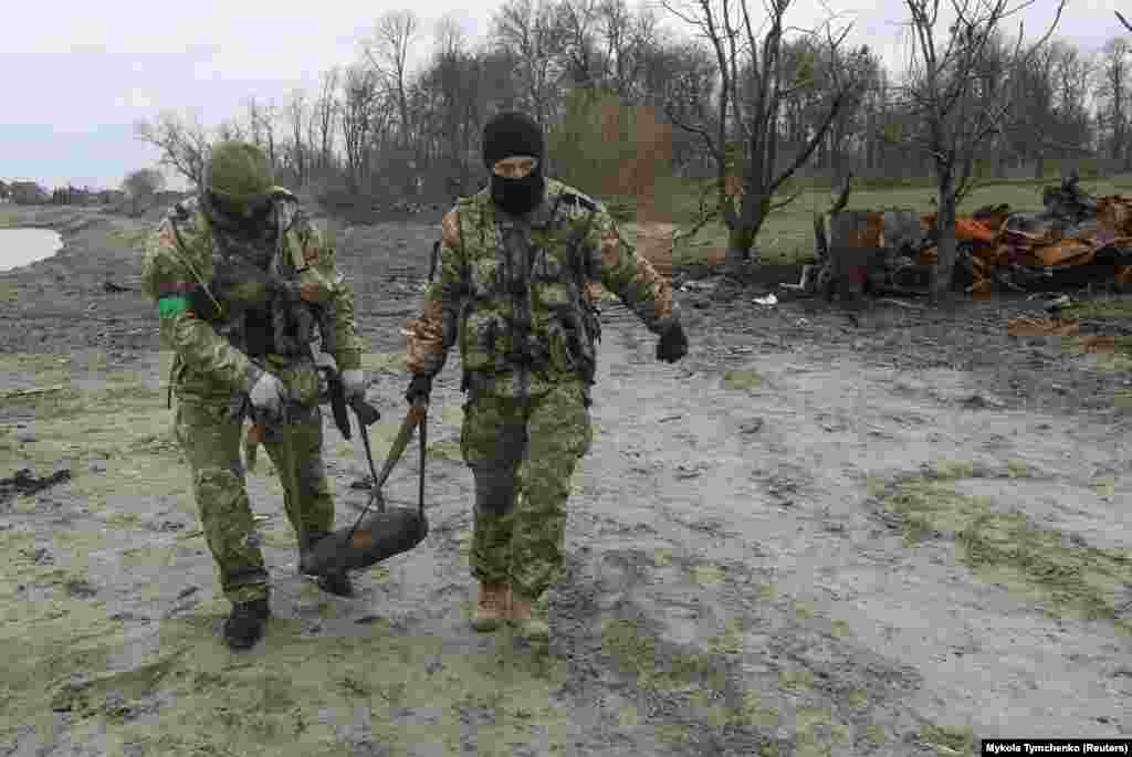 Українські сапери несуть нерозірваний снаряд від знищеного танка біля села Мотижин на захід від Києва, 10 квітня 2022 року