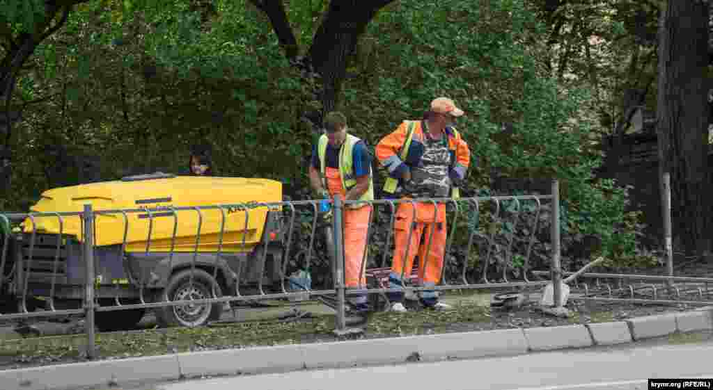 За допомогою відбійного молотка демонтується залізний парканчик у сквері Миру